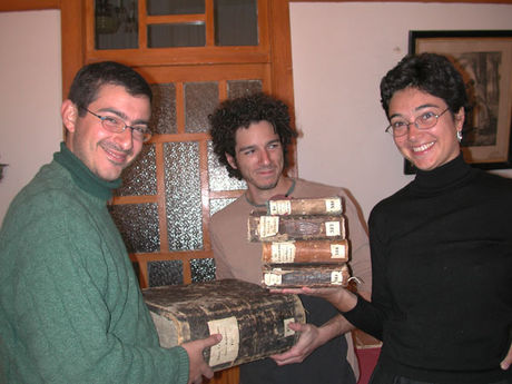 Silvia Pugliese holding 4 small books and Nikolas Sarris and Marco di Bella holding 1 huge book